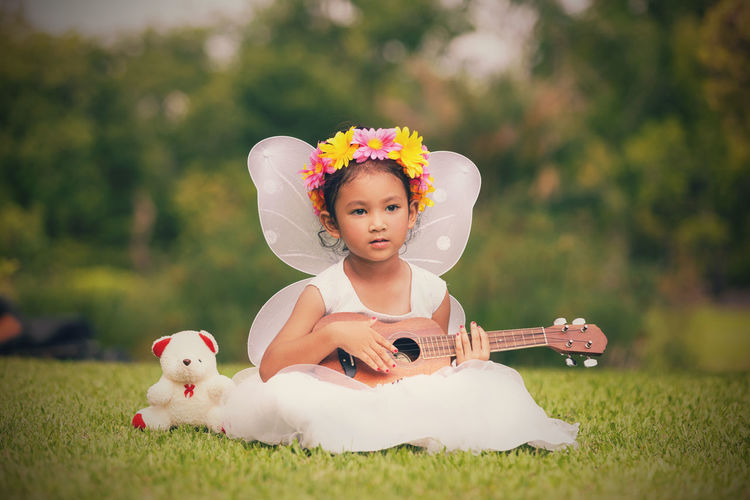 Cute girl looking away while sitting with ukulele on grass