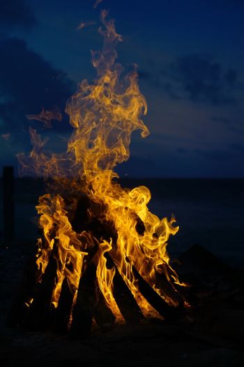 Close-up of bonfire in sea against sky at night