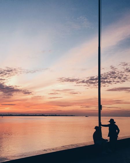 Silhouette people photographing sea against sky during sunset