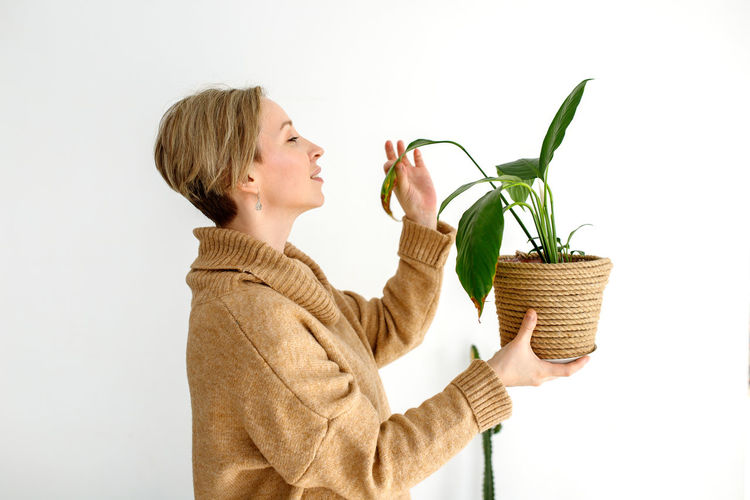 Side view of woman holding potted plant against white background