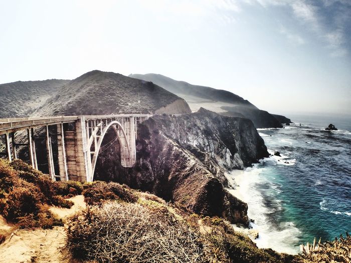 Arch bridge amidst mountains over sea against sky