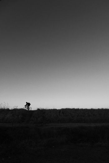 Man riding bicycle on field against clear sky