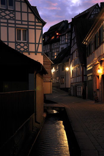 Buildings by empty street against sky at dusk