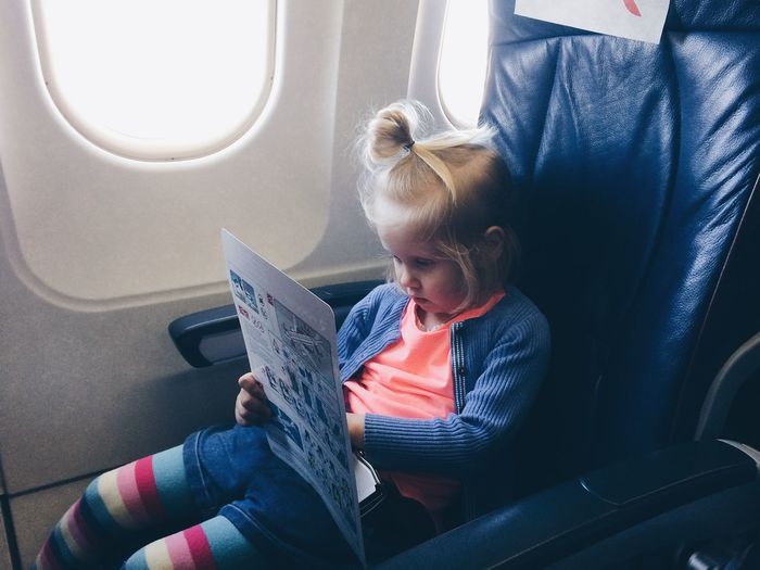 Girl reading chart while sitting by window in airplane