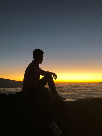 Side view of silhouette man sitting on the top of the mountain against sky during sunset, thinking