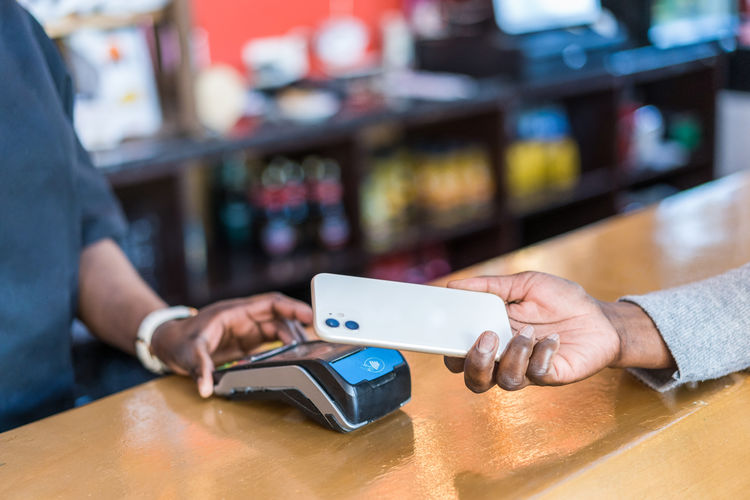 Crop black person making purchase with mobile phone on pos terminal in bar