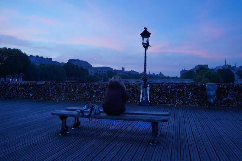 Rear view of woman sitting on bench over pont des arts at dusk