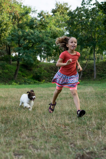 Full length of girl running with dog on grass