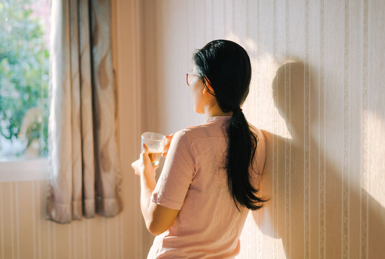 Rear view of woman holding tea cup at home