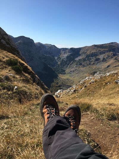 Low section of man on grass against mountains and sky
