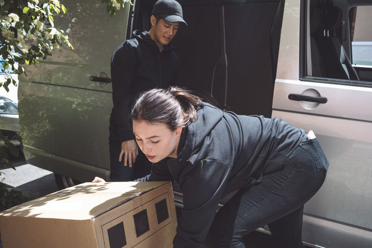 Male and female delivery workers arranging package outside truck