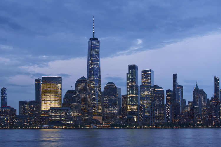 One world trade center by hudson river in city at dusk