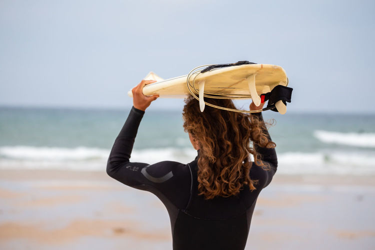 Rear view of man carrying surfboard at beach