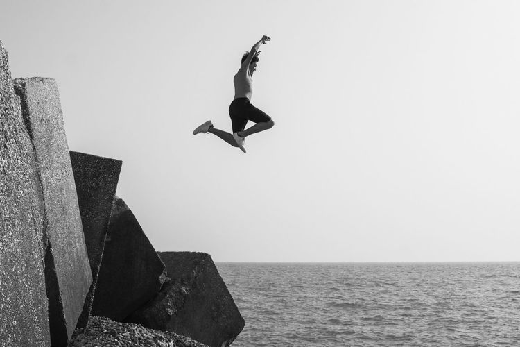 Low angle view of man jumping over sea against clear sky