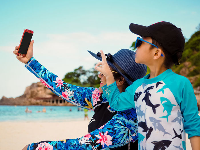 Woman and boy photographing with mobile phone at beach