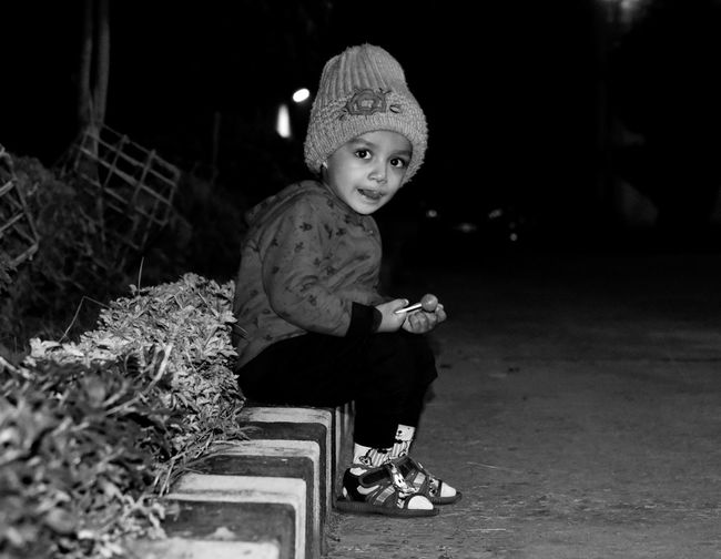 Portrait of boy in warm clothing sitting on curb at night