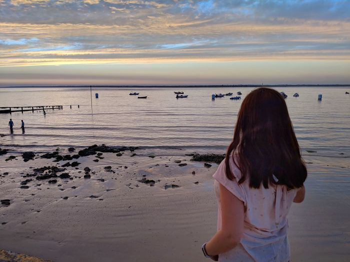 Rear view of woman standing at beach against sky during sunset