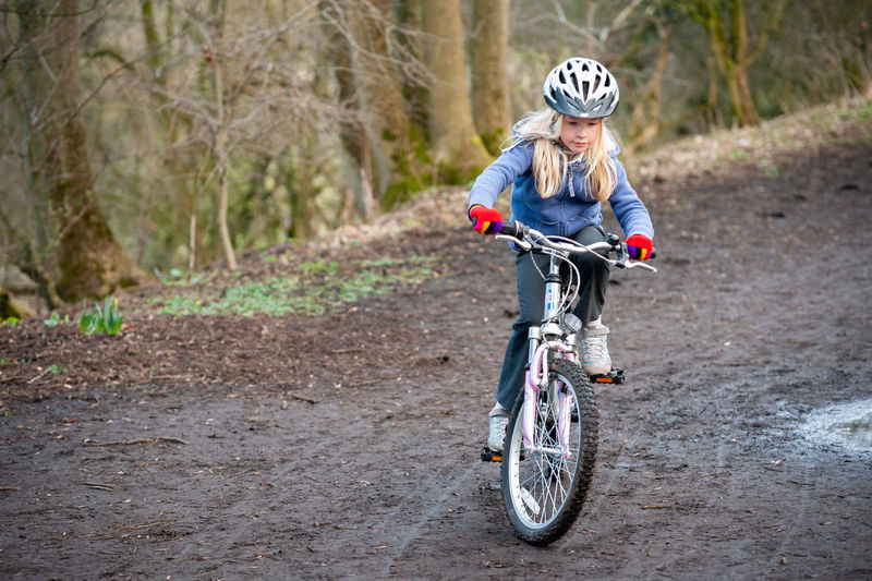 Girl riding bicycle on dirt road in forest