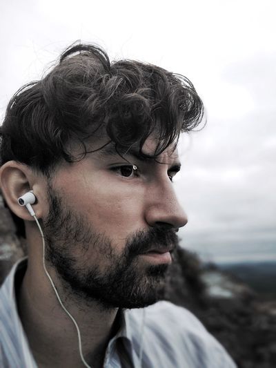 Close-up of mid adult man listening music against sky