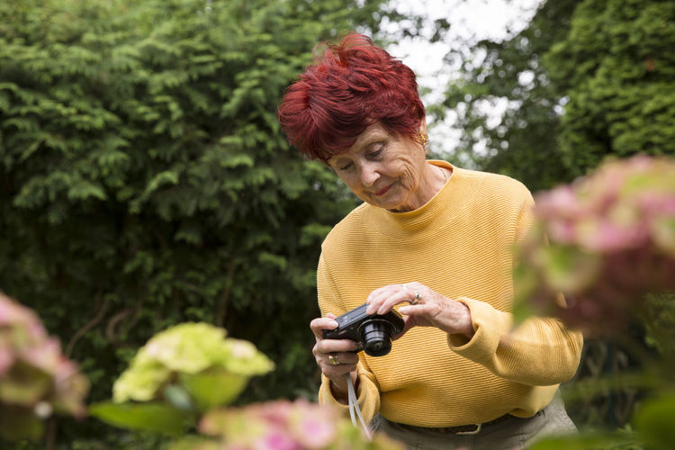 Portrait of old woman standing and using camera 