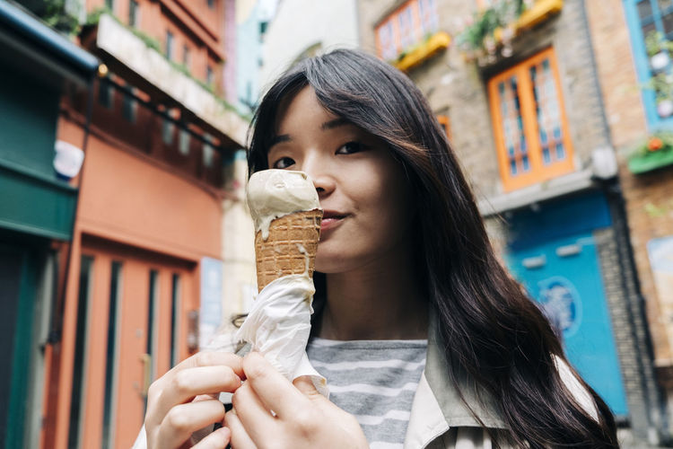 Young woman with ice cream cone in front of buildings