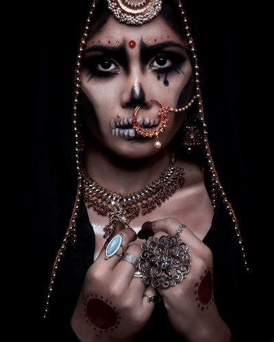 Portrait of young woman in traditional clothing with spooky make-up against black background