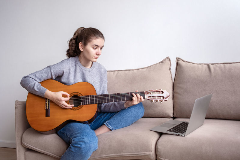 Young man playing guitar while sitting on sofa at home