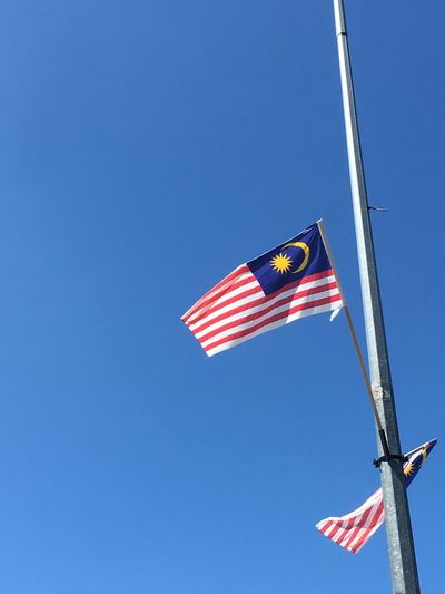 Low angle view of malaysian flags on pole against clear blue sky