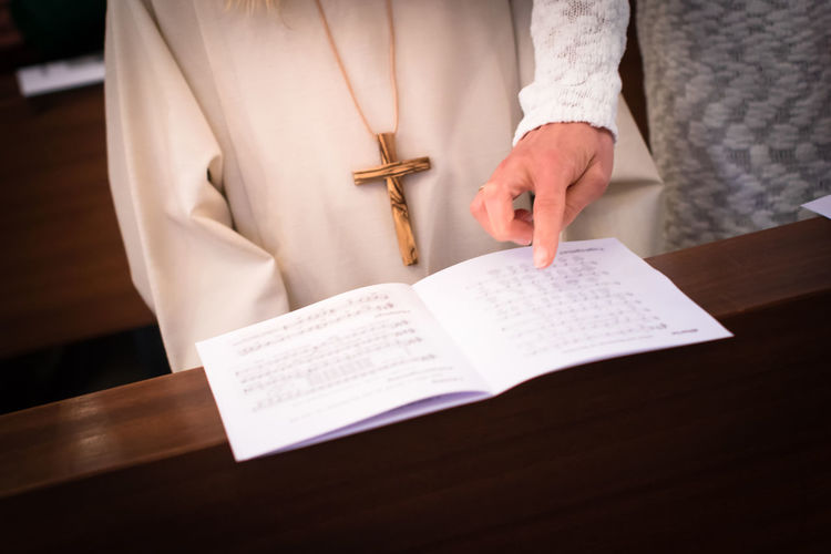 Midsection of mother pointing music sheet by daughter in church during first communion