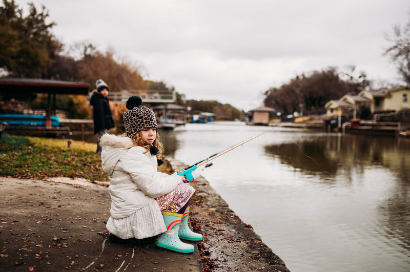 Young girl sitting on rock fishing from backyard dock in winter