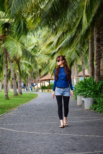 Full length of young woman walking on palm tree