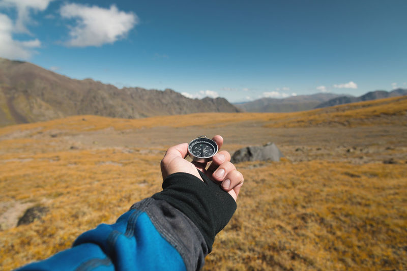 First-person view of a male traveler's hand holding a magnetic compass against 