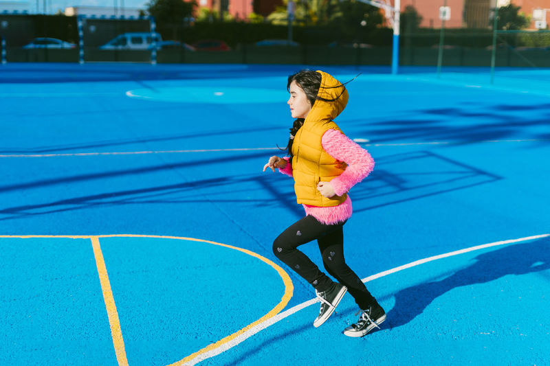 Girl running on blue sports court during sunny day