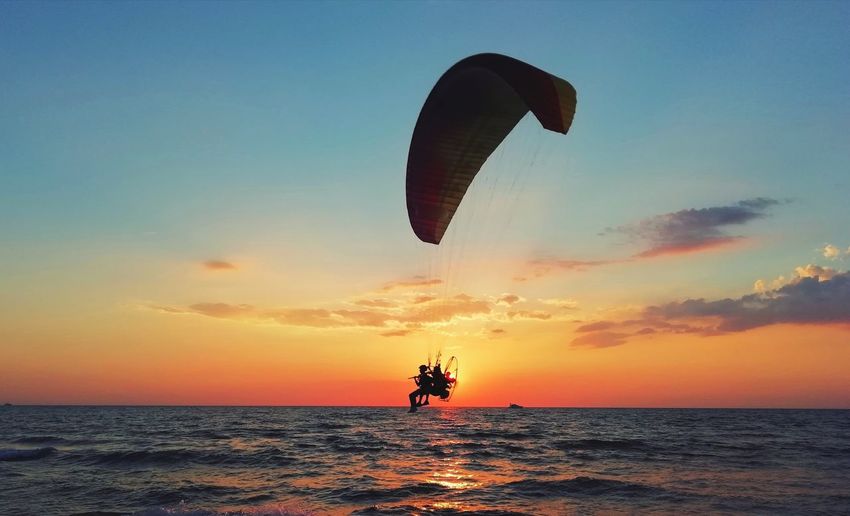 Flight with motorized paraglider over the sea with scenic sunset.
