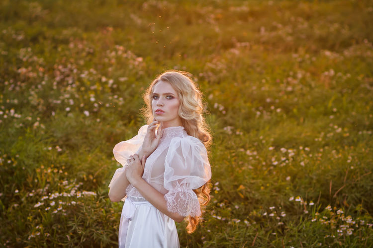 Beautiful young woman wearing white dress while standing on land at sunset