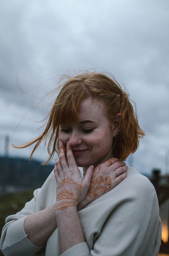 Close-up of smiling young woman standing against cloudy sky