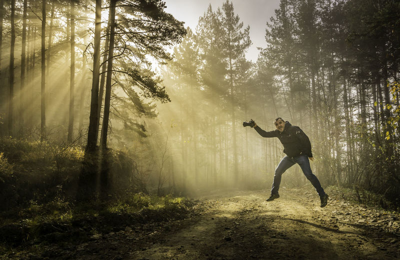Portrait of mature man jumping on road amidst trees at sunset