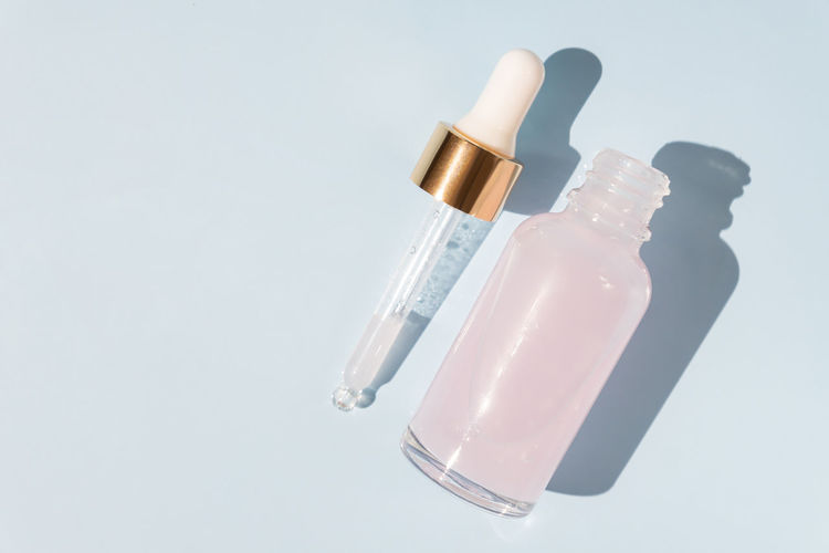 Top view of transparent dropper bottle with pink beauty face oil on blue background. anti aging