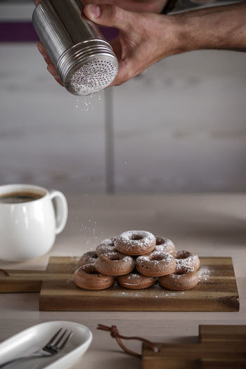Cropped image of man dusting powdered sugar on donuts in kitchen