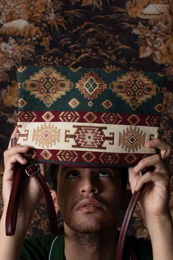 A portrait of a mixed race man holds a bag with tribal pattern.