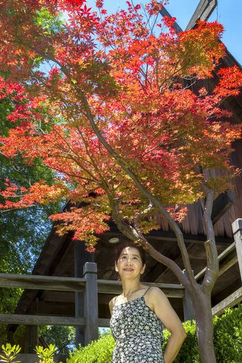 Portrait of young woman standing by tree during autumn