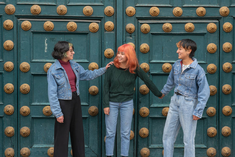 Smiling women friends bonding hands and standing near blue wooden decorated door in cusco city