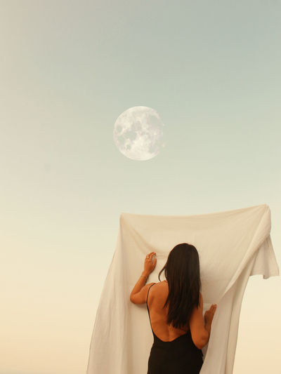 REAR VIEW OF WOMAN STANDING AGAINST MOON