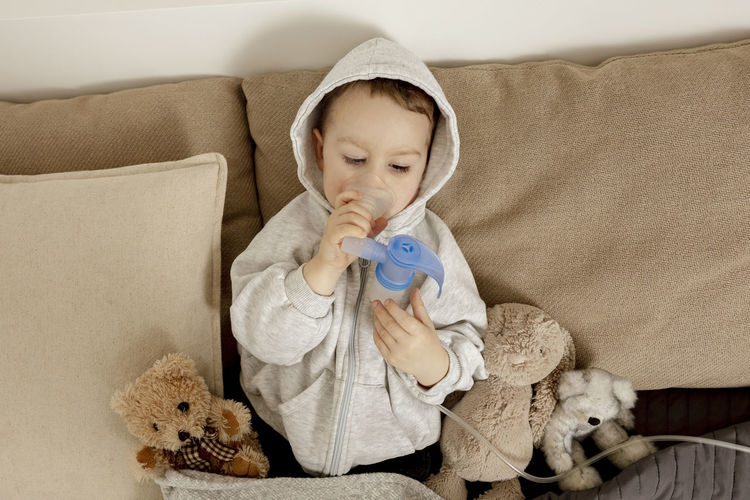Sick little boy with inhaler for cough treatment. unwell kid doing inhalation on his bed. flu season