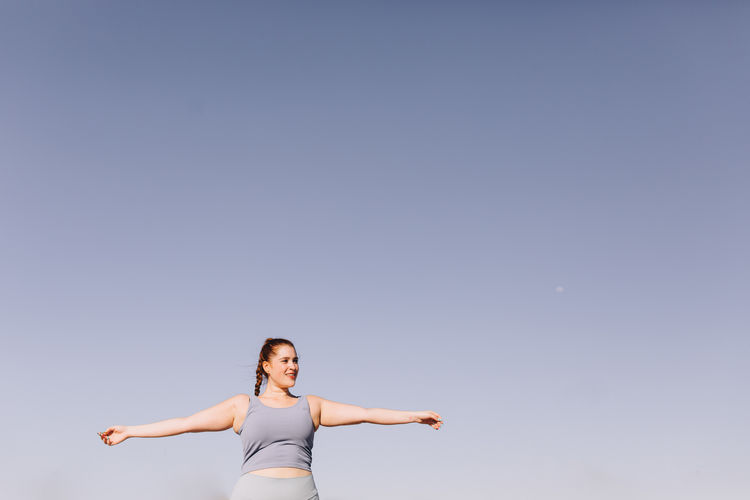 Woman with arms raised against clear sky