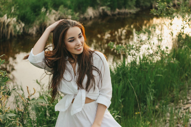Beautiful young woman looking away by plants against river