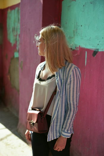 Woman looking away while standing against wall