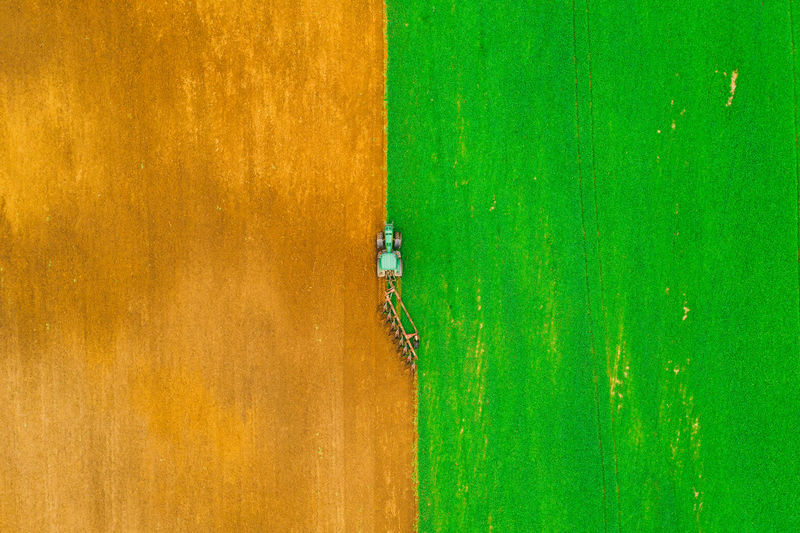 Aerial photo of brown and green field. tractor harrows the ground. vertical pattern.