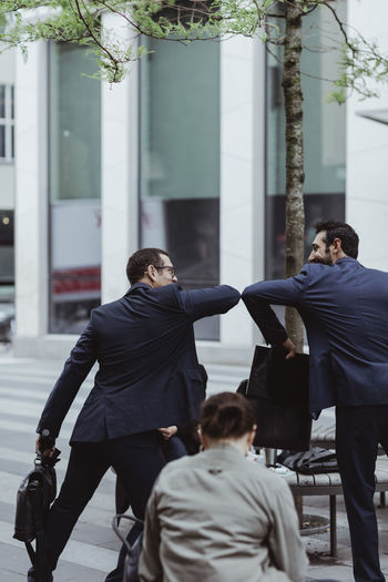 Rear view of entrepreneurs greeting each other with elbow bump in city