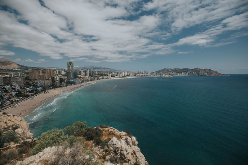 View of city at waterfront against cloudy sky